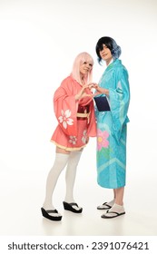 happy young cosplayers in colorful kimonos showing heart sign with hands on white, anime style