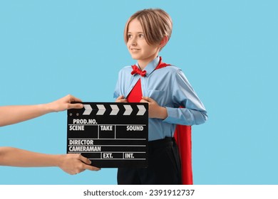 ممثل صغير يرتدي زي بطل خارق ويده تحمل مصفقًا سينمائيًا على خلفية زرقاء