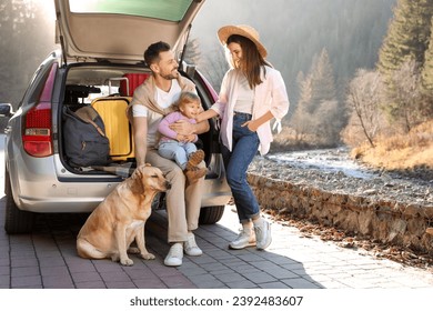 Orang tua, putri mereka, dan anjing di dekat mobil di luar ruangan. Keluarga bepergian dengan hewan peliharaan