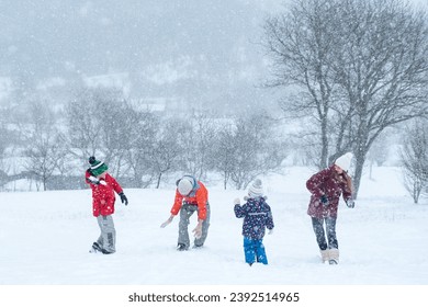 Big family with children play snowballs outside during snowfall. Winter fun holidays. Games in winter outdoors