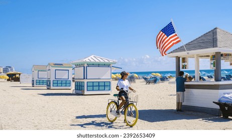 Junge Frauen mit Fahrrädern am Strand in Miami, ein farbenfroher Strand in Miami und eine Rettungsschwimmerhütte in South Beach, Florida. Asiatische Frauen fahren mit Fahrrädern am Strand