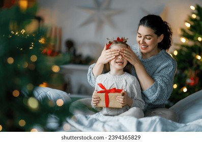 Selamat Natal dan Selamat Hari Raya. Ibu yang ceria dan putrinya yang manis saling bertukar hadiah. Orang tua dan anak kecil bersenang-senang di dekat pohon di dalam ruangan. Keluarga yang penuh kasih dengan hadiah di dalam ruangan.