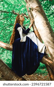 Elfia wojowniczka w niebieskiej sukni i rudych włosach w lesie.