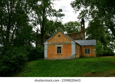 Крупним планом покинута хатина, халупа чи цегляний будинок, розташовані поруч із руїнами старої церкви посеред густого лісу чи трясовини, поруч із великим полем, лугом чи пасовищем
