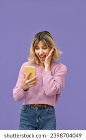 Jovem loira da geração Z animada com smartphone, estudante cliente feliz parecendo impressionada usando celular comemorando o prêmio online em fundo roxo, vertical.