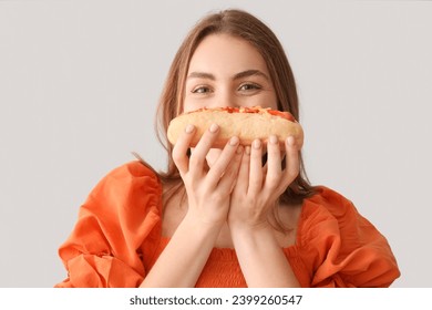 Pekná mladá žena s chutným hot dogom na sivom pozadí