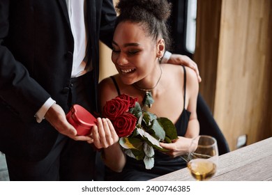 gentleman gifting heart-shaped box to happy african american woman with roses on Valentine`s day