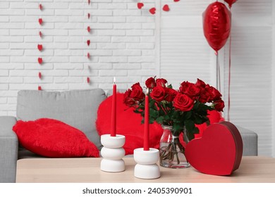 Bouquet of beautiful roses with gift box and candles on table in room decorated for Valentine's Day celebration