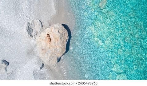 Lijepa žena u bikiniju sunča se na velikoj stijeni na plaži Lalaria u Skiathosu