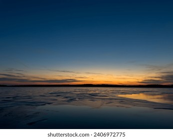 Scenic view of a frozen lake on a cold November night with a colorful sunset and the horizon in the background.