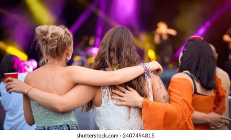 มุมมองด้านหลังของเพื่อนสาวสามคนกำลังเต้นรำในเทศกาลดนตรีฤดูร้อน
