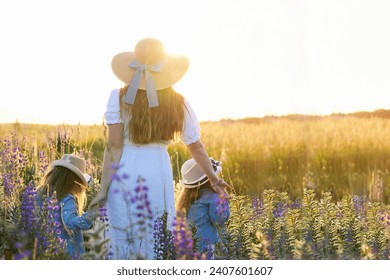幸せなお母さん。ルピナスが咲く草原を散歩する双子の娘を持つ若い女性。コピースペース。