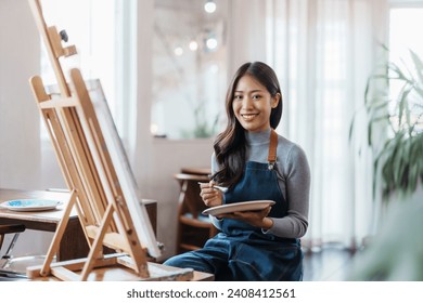 Artistă femeie asiatică fericită desenând o poză pe pânză în studio.