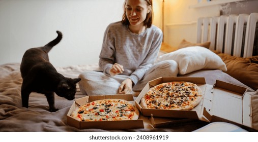 wanita kesepian di rumah dengan seekor kucing memesan dua pizza. Makan pizza di tempat tidur di rumah.