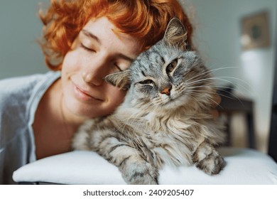 gadis remaja dengan rambut merah keriting, dengan hewan peliharaan, kucing berbulu besar bergaris abu-abu, menghabiskan waktu bersama.