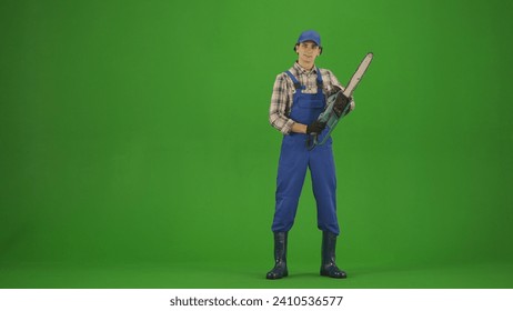 Retrato de un granjero con ropa de trabajo en una pantalla verde con efecto croma. Un jardinero posando para la cámara con una motosierra en la mano.