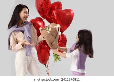 Little Asian girl greeting her mother with Valentine's day on white background