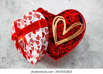 Saint Valentin. Des roses rouges et des coeurs dorés dans une boîte en forme de coeur sur un fond en béton. Un cadeau pour les femmes en vacances. Le concept de livraison de fleurs. fleuristerie et fleuristes.