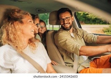 Mother, father and their two daughters are sitting in the car and driving away for the weekend to spend quality time together. Portrait of a happy family traveling together. Copy space.