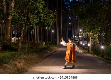 Perkhemahan kanak-kanak Asia atau kanak-kanak perempuan mengembara berkhemah dan berdiri sambil memegang tanglung putih hangat atau lampu bersendirian pada malam senja di resort taman pokok alam semasa bercuti di Taman Hutan Doi Bo Luang