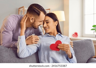 Glücklich lächelnde Menschen in der Liebe küssen sich, geben rotes Papierherz und teilen einen besonderen romantischen Moment. Valentinstag-Emotion, glückliches Familienpaar, Vertrauen zwischen Liebespaaren, Respekt zwischen Partnern