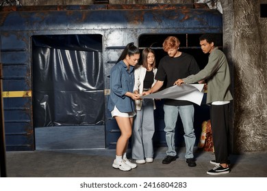 group of young multicultural friends solving mystery while looking at map in escape room, quest