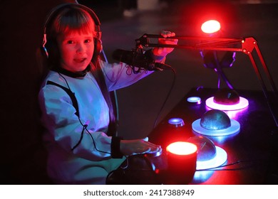 Europees meisje van 8 jaar oud in kosmonautenkostuum met planeten in rood licht, sprekende microfoon