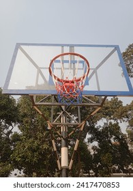 Basketballkorb mit Netz und weißem Backboard für Basketballspiel im Freien mit grünen Bäumen und blauem Himmel im Hintergrund. Fotoshooting bei Tageslicht in Bangladesch.