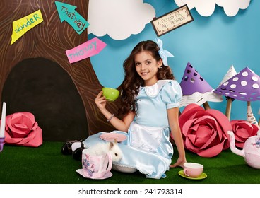 Cô bé xinh đẹp với mái tóc dài gợn sóng trong chiếc váy lụa xanh trong khung cảnh Alice ở xứ sở thần tiên với chú thỏ bông trắng phiêu lưu trong câu chuyện cổ tích