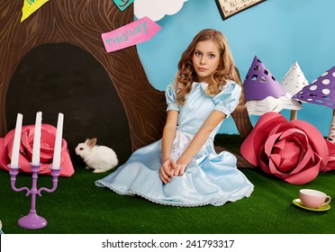 Cô bé xinh đẹp với mái tóc dài gợn sóng trong chiếc váy lụa xanh trong khung cảnh của Alice ở xứ sở thần tiên với chú thỏ bông trắng phiêu lưu trong câu chuyện cổ tích