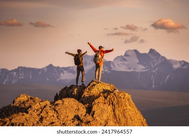 Zwei glückliche junge Touristen mit Rucksäcken stehen mit offenen Armen auf dem Berggipfel und genießen den Blick auf den Sonnenuntergang