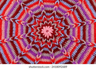 En Element vun engem gestrickte Teppech aus faarwege Wollfäden. Gestrickten Hannergrond, Mandala. Handgemaach, Musterbeispill, Hobby, Online-Cours iwwer modesch Stricken, Ritualsaachen, gestrickte Bannenariichtungen.