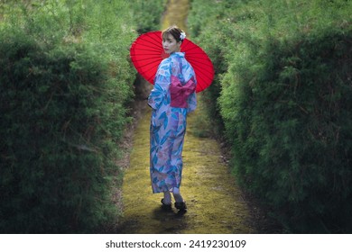Jolie fille en robe Yukata. Une jeune femme asiatique portant un kimono traditionnel japonais ou une robe Yukata et tenant un parapluie rouge est heureuse et détendue dans l'atmosphère de la nature verte et fraîche.