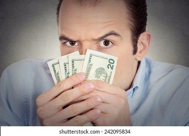 Closeup portrait greedy banker executive CEO boss, corporate employee funny looking man holding dollar banknotes scared to loose money, suspicious isolated grey background. Human face expression
