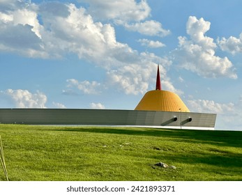 ふわふわの白い雲と明るい緑の草が広がる青い空を背景にした国立コルベット博物館。
