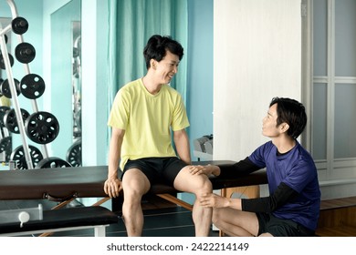 Paciente do sexo masculino conversando com quiroprático asiático dando massagem quiroprática esportiva