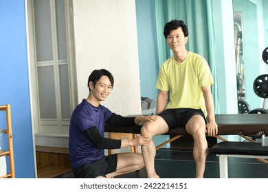 Paciente do sexo masculino conversando com quiroprático asiático dando massagem quiroprática esportiva