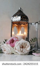 Lanterna marocană de argint, arabă cu lumânare aprinsă. Flori de trandafiri roz pe masa albă. Natură moartă festivă pentru sărbătoarea musulmană Ramadan Kareem sau nuntă boho, fundal neclar, vertical.