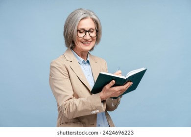 Portrait smiling senior woman, writer holding notepad, taking notes, planning new book isolated on blue background. Confident manager brainstorming, working. Successful business concept