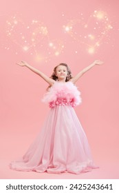 Uma linda garotinha com cabelos cacheados e um longo vestido de noite rosa com penas posa em um fundo rosa festivo com corações brilhantes. Moda infantil de férias. Princesinha.