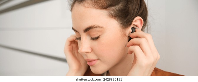 Chân dung cận cảnh một người phụ nữ dịu dàng, tươi cười và dễ thương, đang đeo tai nghe không dây màu đen vào tai, đang nghe nhạc.