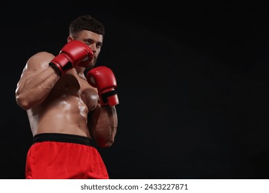 Hombre con guantes de boxeo peleando sobre fondo negro. Espacio para texto