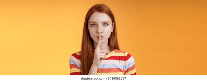 Girl hides lots secrets. Serious-looking redhead girlfriend blue eyes demand keep silent voice down show shhh shush gesture index finger pressed lips, prepare surprise, orange background.