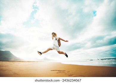 Happy traveler with hands up jumping at the beach - Delightful man enjoying success and freedom outdoors - Wanderlust, wellbeing, travel and summertime holidays concept