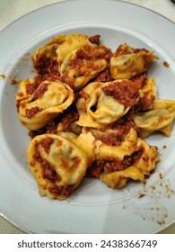 In the white dish there are tortelloni with meat sauce, a typical food of Modena, Emilia Romagna (Italy): pasta filled with ricotta and spinach and seasoned with meat sauce, all homemade.