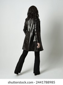 Full length portrait of brunette woman wearing long leather trench coat and black boots. Standing pose walking away from camera, facing backwards. Isolated silhouette on white studio background.