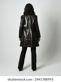 Full length portrait of brunette woman wearing long leather trench coat and black boots. Standing pose walking away from camera, facing backwards. Isolated silhouette on white studio background.