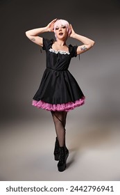 privlačna šik žena u crnoj haljini s ružičastom kosom koja cosplayira anime lik i gleda u kameru