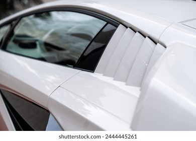 Ausschnitt aus weißem Lamborghini mit durchdachtem Detaildesign. Reflektierendes Glas auf der Fahrerseite mit Blick auf Lenkrad und Innenraum