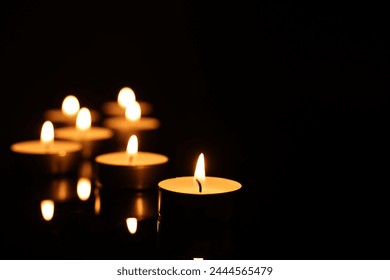 Burning candles on mirror surface in darkness, closeup. Space for text